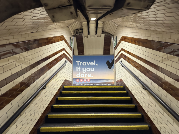 Eine Treppe in einer U-Bahn-Station mit einem "Reise, wenn du wagst"-Schild oben, flankiert von Geländern und StationWsänden im Hintergrund.
