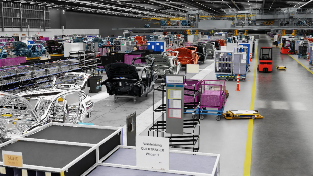 Gro├če Fabrik mit mehreren Autos auf einer Fließbandlinie, Metallstrukturen an den Seiten, Fahrzeuge auf dem Boden, eine Wand im Hintergrund und Deckenleuchten, mit "Volkswagen"-Text, der den Standort der Anlage angibt.