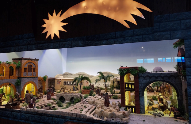 Eine Krippe-Ausstellung im Museum mit Menschen, Tieren, Häusern, Bäumen und anderen Gegenständen und einer beleuchteten Hintergrundatmosphäre.