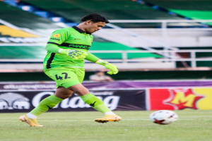 Ein Torwart in einem grünen Trikot schießt einen Fußball auf einem Rasenfeld in einem Stadion, mit Bannern im Hintergrund, die "Chivas USA vs Mexico City, 3-1, Copa Libertadores" anzeigen.