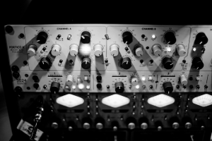 Ein Schwarz-Weiß-Foto eines analogen Synthesizers auf einem Tisch, mit verschiedenen Knöpfen, Schaltern und einem angeschlossenen Kabel.