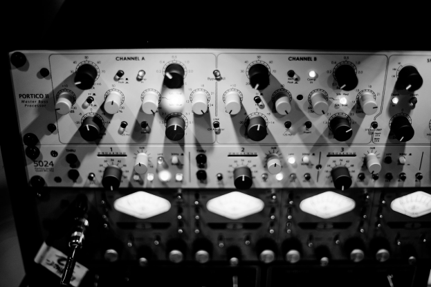 Ein Schwarz-Weiß-Foto eines analogen Synthesizers auf einem Tisch, mit verschiedenen Knöpfen, Schaltern und einem angeschlossenen Kabel.