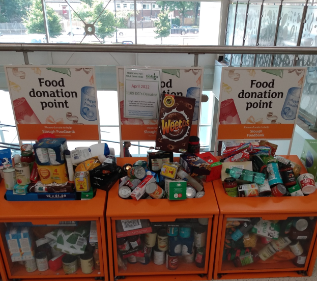 Orange Schränke mit Lebensmitteldosen, -dosen und -kartons gefüllt, mit Informationsschildern im Hintergrund; Glasfenster zeigen Fahrzeuge, Bäume, Gebäude und Himmel.