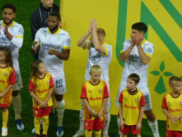 Eine Gruppe von Fußballspielern in Uniformen, die auf einem Ligue-1-Feld klatschen und einen Sieg feiern.