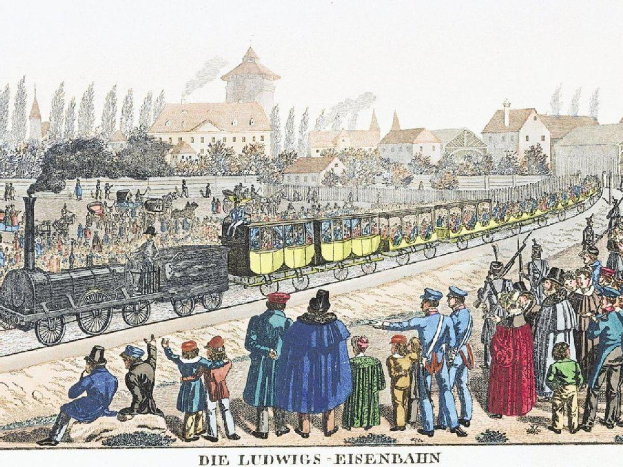Eine Gruppe von Menschen steht um einen Zug auf einem Gleis herum, einige sitzen im Zug und andere stehen daneben, in der Nähe von Gebäuden und Bäumen, mit dem Text "Ludwigs-Eisenbahn, der erste Bahnhof Deutschlands" unten.