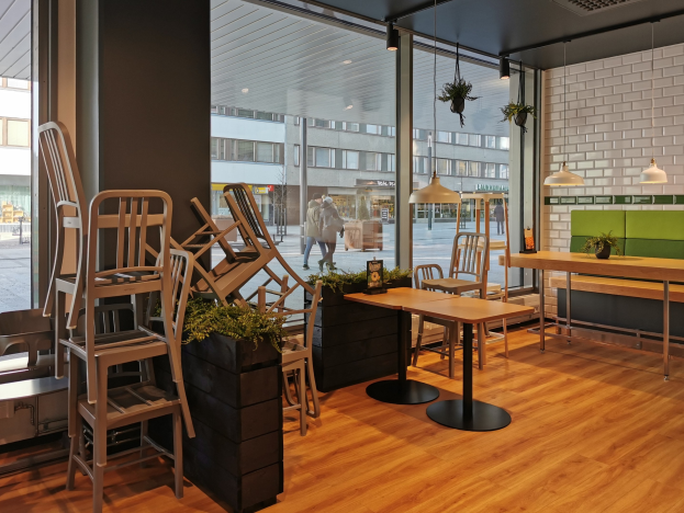Ein Berliner Restaurant mit Holztischen und -stühlen vor einem großen Fenster, das städtische Elemente wie Fußgänger, Gebäude und Straßenmöbel zeigt.