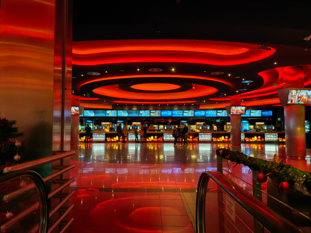 Ein Casino-Inneneinrichtung mit einem Weihnachtsbaum in der Mitte, gefliestem Boden, Geländern auf beiden Seiten, verzierten Säulen und Deckenleuchten, mit Menschen im Hintergrund, die eine festliche Atmosphäre schaffen.
