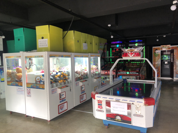 Ein Raum voller verschiedener Arcade-Spiele, mit einem Spielautomaten auf der rechten Seite, einem sichtbaren Boden und Deckenleuchten.