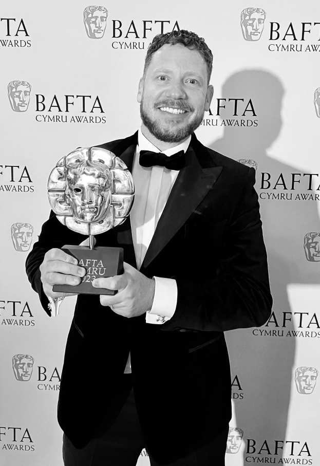 Ein Mann im Smoking mit einem BAFTA-Award, der vor einer Tafel mit der Aufschrift "BAFTA Awards 2018" steht.