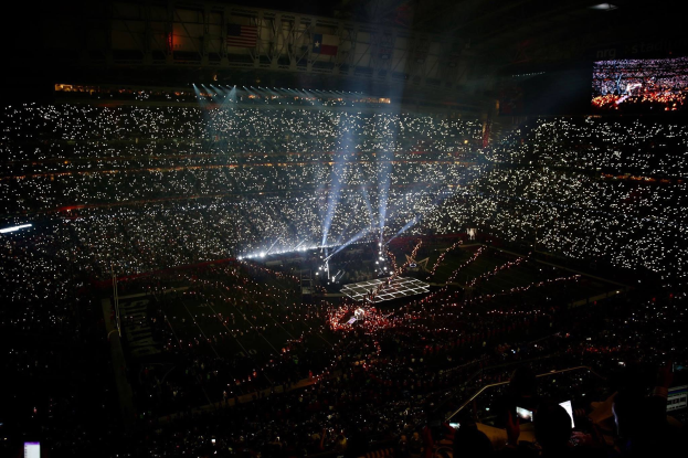 Gro├če Menschenmenge in hell erleuchtetem Stadion bei Nacht mit einem Bildschirm, der rechts die Ergebnisse der Super Bowl XLVII-Halbzeitshow anzeigt.