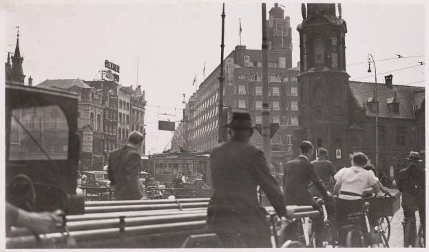 Schwarzes und weißes Foto von Rädern auf einer Straße in Amsterdam im frühen 20. Jahrhundert mit Gebäuden, Masten und Drähten an der Straße.