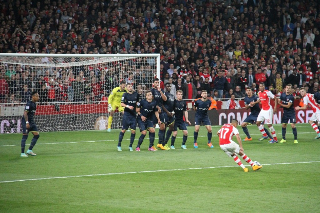 Ein Fußballspiel im Gange mit Spielern auf dem Feld und einer großen Menge im Hintergrund.