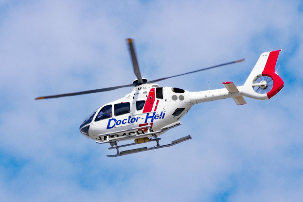 Weißer und roter medizinischer Hubschrauber fliegt durch einen blauen Himmel mit Wolken.