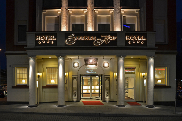 Das Essenerhof Hotel in Berlin, Deutschland, ein mehrstöckiges Gebäude mit Fenstern, Türen, Säulen und einem Namensschild, das entlang einer Straße mit Fahrzeugen auf der rechten Seite und einem klaren Himmel im Hintergrund liegt.