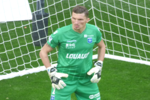 Ein Torwart in grüner Uniform steht vor einem Fußballtor auf saftigem Grün.