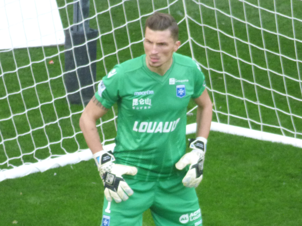Ein Torwart in grüner Uniform steht vor einem Fußballtor auf saftigem Grün.