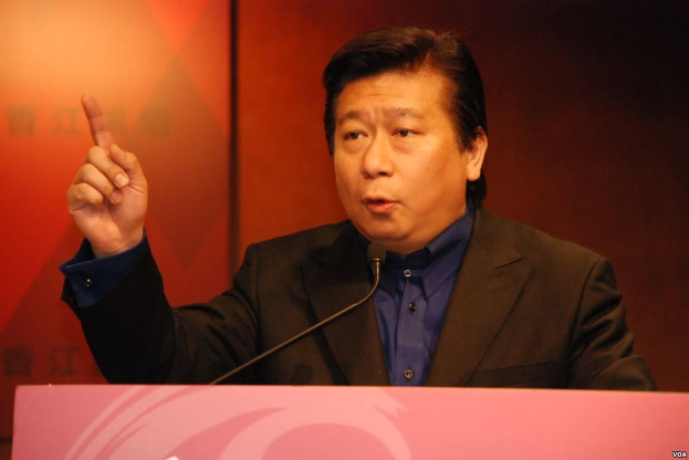 Ein Mann in Anzug und Krawatte, der hinter einem Rednerpult mit Mikrofon spricht und ernst dreinschaut.