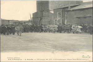 Eine Gruppe von Männern, die eine Straße entlanggehen, die von Gebäuden gesäumt ist, unter einem klaren Himmel, mit dem Text "Voyage de Mr Clémenceau dans les Ardennes" unten.