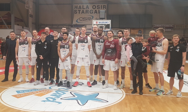 Gruppe von Männern und Kindern auf einem Basketballfeld mit Schildern im Hintergrund, die "Hala Osir Starga" lesen.