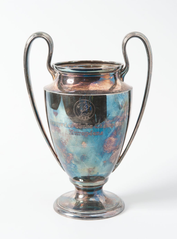 Der UEFA-Champions-League-Pokal, ein stählerner Becher mit zwei Griffen und einem blauen und silbernen Farbschema, der mit 'UEFA Champions League' beschriftet ist, vor einem weißen Hintergrund dargestellt.