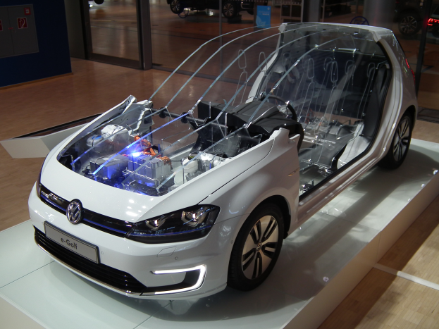 Ein weißer Volkswagen e-Golf-Elektroauto auf der IAA in Frankfurt, umgeben von Glastüren und anderen Fahrzeugen im Hintergrund.