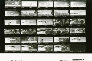 Schwarzes und weißes Foto eines konzentrierten Mannes in einem weißen Hemd und Shorts, der Tennis spielt und einen Schläger hält, mit einem Filmstreifen-Hintergrund.