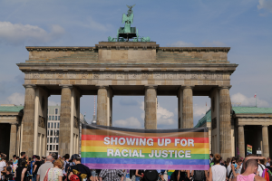 Eine Gruppe von Menschen, die vor dem Brandenburger Tor in Berlin, Deutschland, mit einem Banner mit der Aufschrift "Racial Justice" stehen.