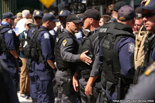 Eine Gruppe von Polizisten in Uniform, die auf einer Straße stehen, einige mit Waffen, vor Gebäuden und Schildern im Hintergrund.