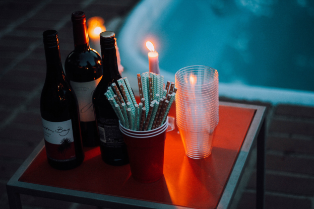 Ein Tisch am Swimmingpool mit zwei Weinflaschen, einer Kerze, Gläsern und Strohhalmen, der eine entspannte Nacht am Pool verspricht.