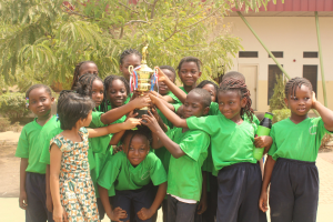 Gruppe von Kindern mit einem Pokal in einem Schulhof mit Bäumen und einem Gebäude im Hintergrund
