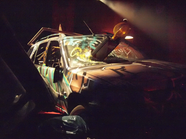 Ein verunglücktes Auto am Straßenrand in einer dunklen Gegend, mit seinem Rad und Reifen sichtbar.