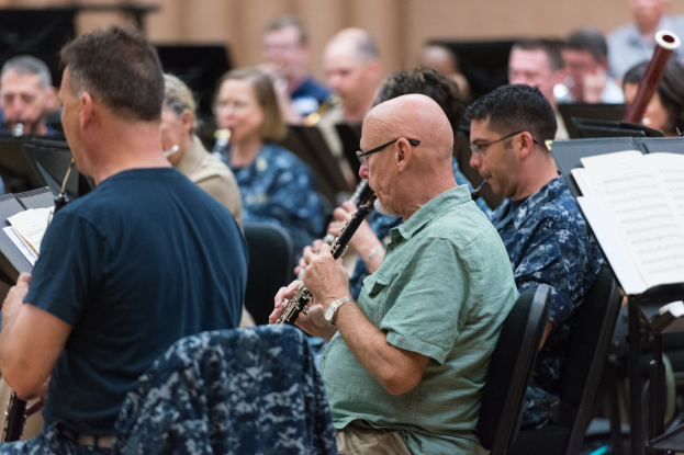 Eine Gruppe von Männern, die Klarinetten in einem Raum mit Notenpulten spielen.
