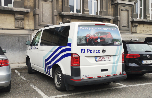Ein Polizeiwagen steht auf einem Parkplatz neben einem Gebäude mit Fenstern, umgeben von anderen Fahrzeugen auf der Straße.