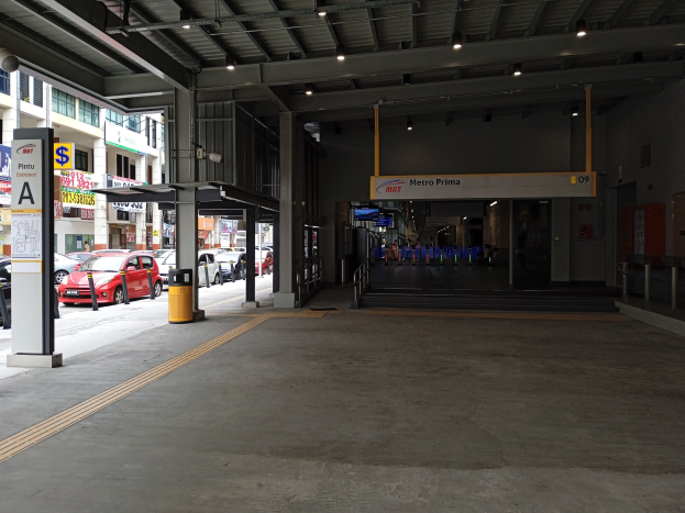 Leeres Parkhaus mit geparkten Autos, Betonpfeiler, Informationsschilder, Deckenbeleuchtung und Gebäuden mit Fenstern im Hintergrund.