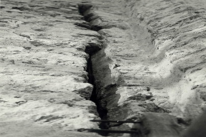 Schwarzes und weißes Foto eines großen Risses im Boden, wahrscheinlich ein Entwässerungsgraben, mit einem sichtbaren Wasserzeichen auf der linken Seite.