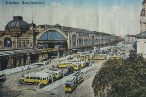 Eine sepiafarbene Postkarte des Dresdner Hauptbahnhof Bahnhofs in Deutschland, die eine belebte Straße mit Fahrzeugen, Fußgängern, Bäumen und Gebäuden unter einem bewölkten Himmel zeigt.